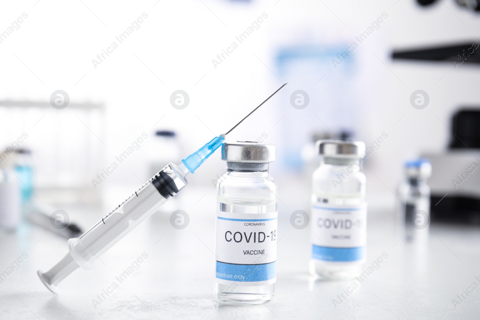 Photo of Vials with vaccine against Covid-19 and syringe on white table indoors