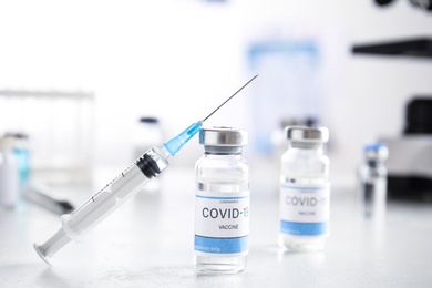 Photo of Vials with vaccine against Covid-19 and syringe on white table indoors