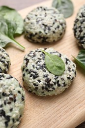 Photo of Tasty vegan cutlets with sesame seeds and spinach on wooden board, closeup