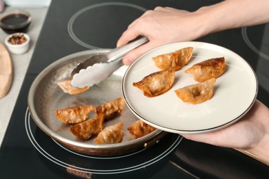 Photo of Woman serving freshly cooked delicious gyoza on plate in kitchen, closeup