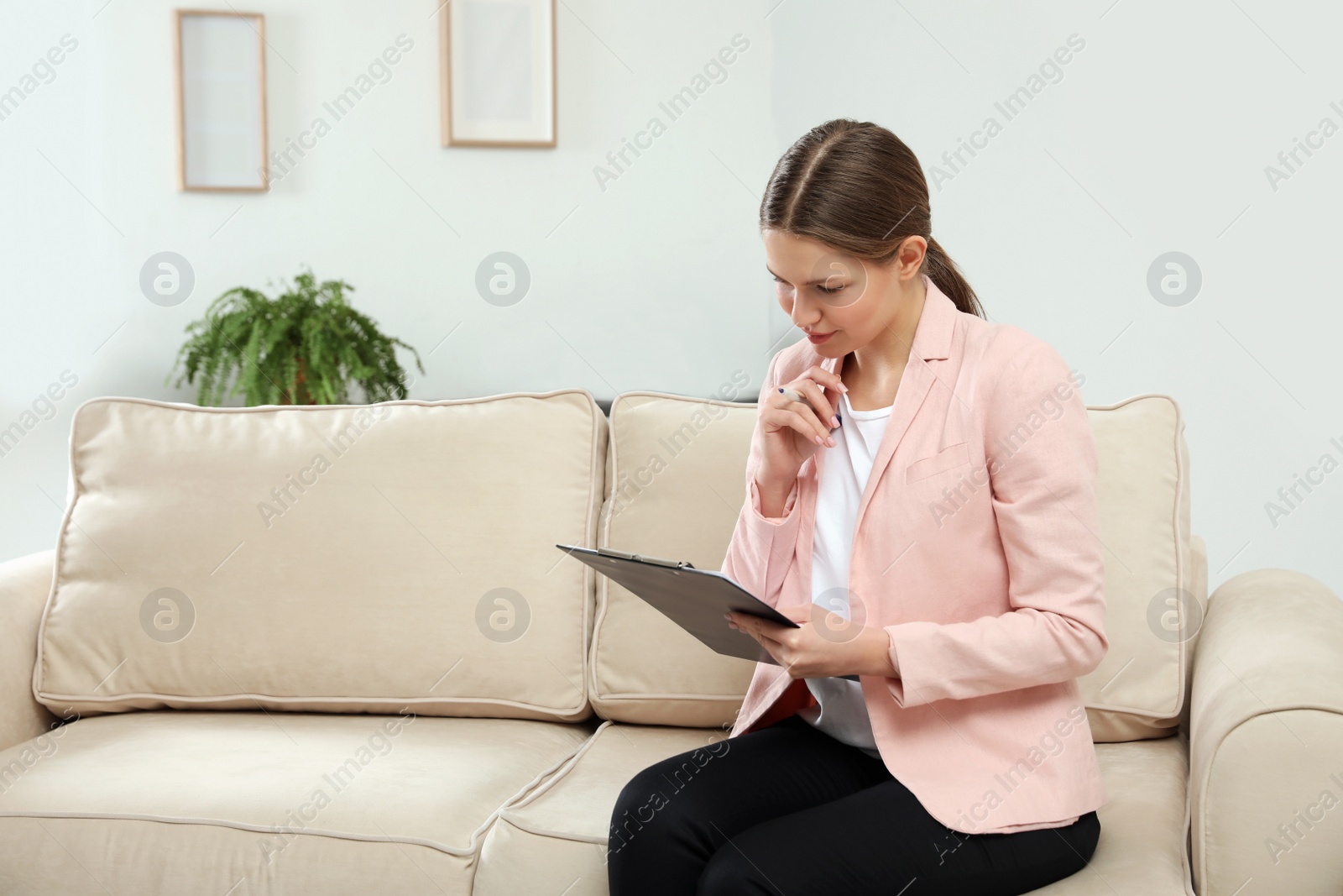 Photo of Professional psychotherapist with clipboard on sofa in office