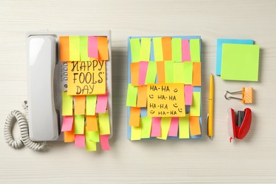 Photo of Corded phone and notebook covered with sticky notes on wooden table, flat lay. April fool's day celebration