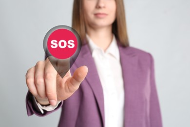 Young woman pressing virtual SOS button in case of danger on grey background, closeup