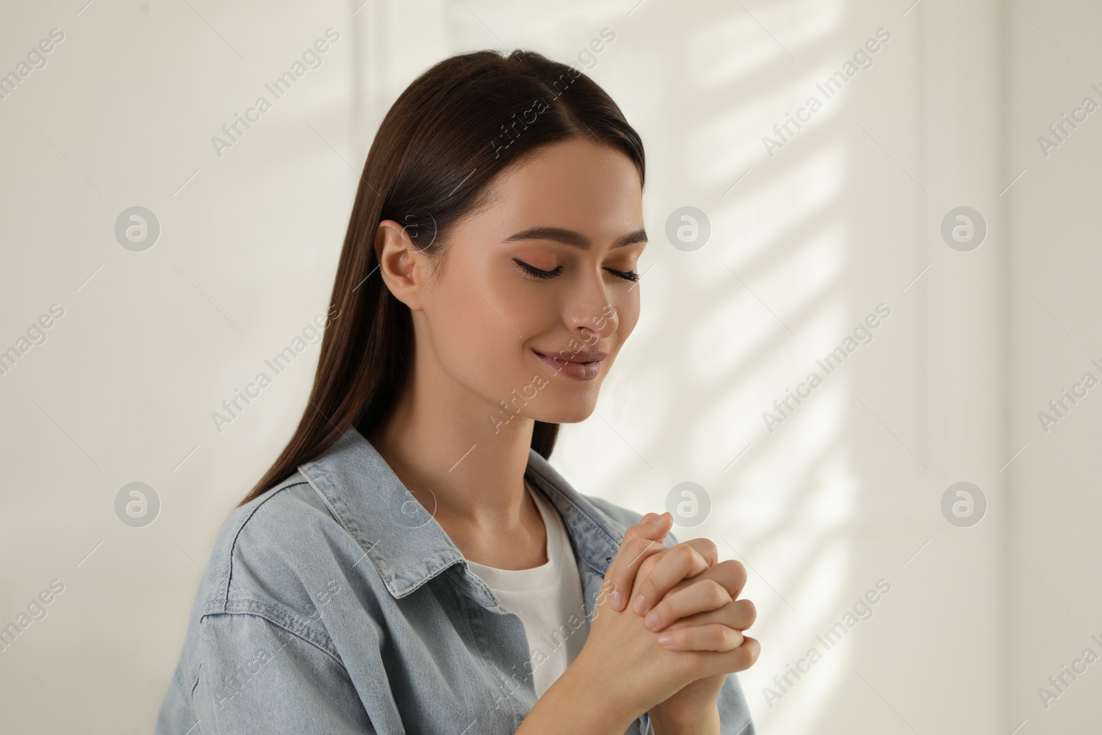 Photo of Religious young woman with clasped hands praying indoors