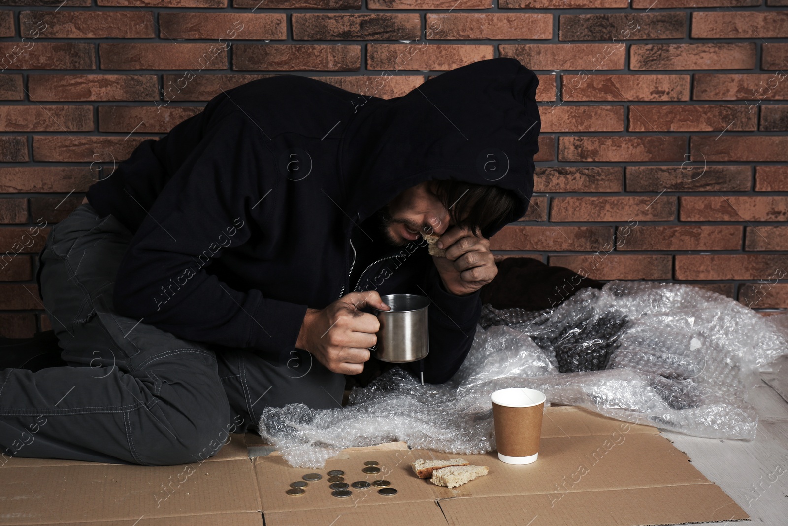 Photo of Poor man with piece of bread and mug near brick wall