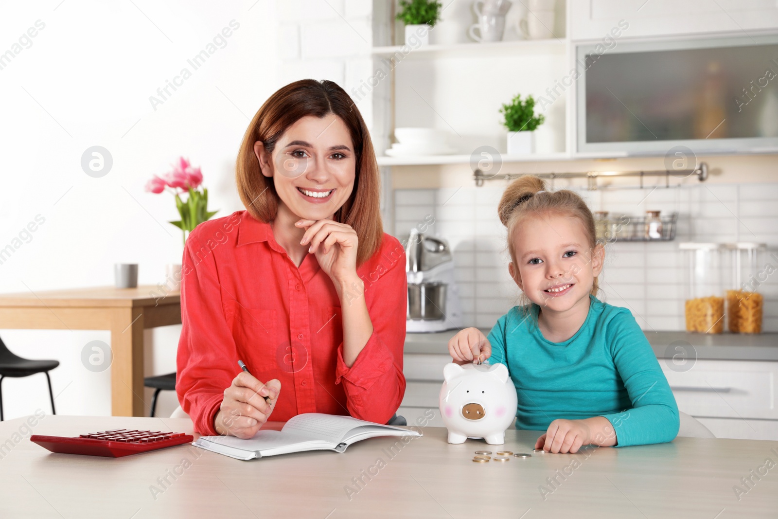 Photo of Mother and daughter putting coin into piggy bank at table indoors. Saving money