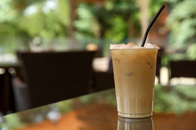 Photo of Plastic takeaway cupdelicious iced coffee on table in outdoor cafe, space for text