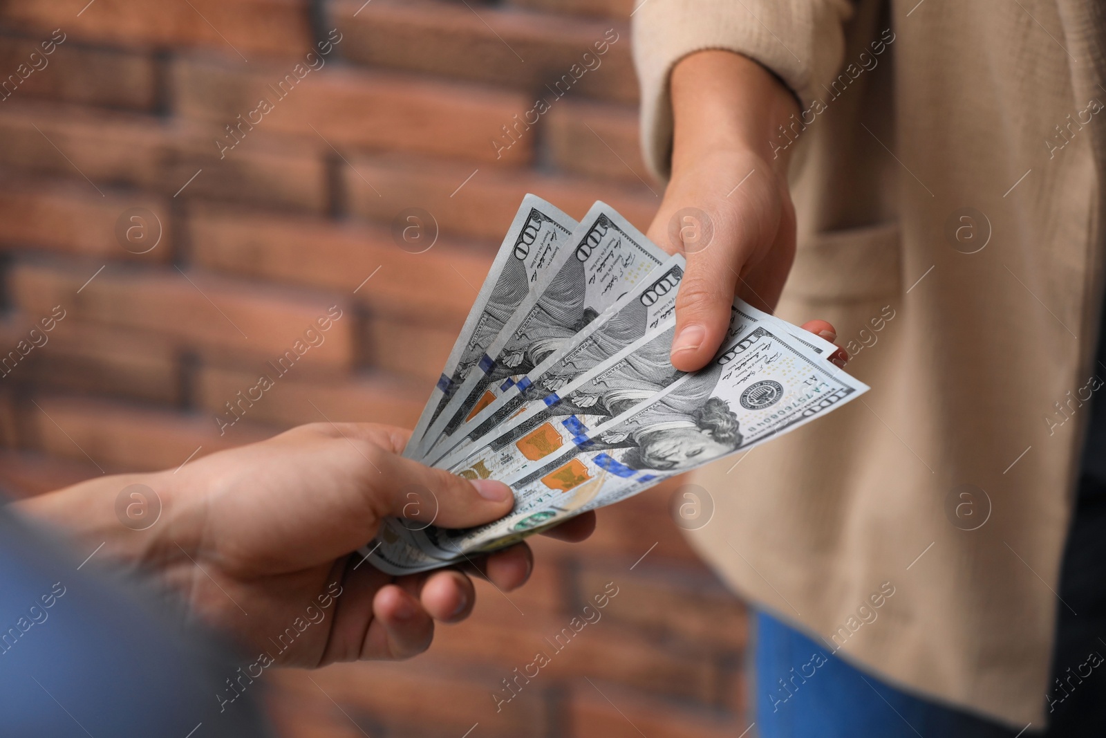 Photo of Man giving woman American money near brick wall, closeup