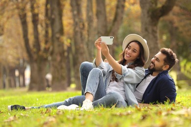 Photo of Beautiful young couple taking selfie in park. Space for text