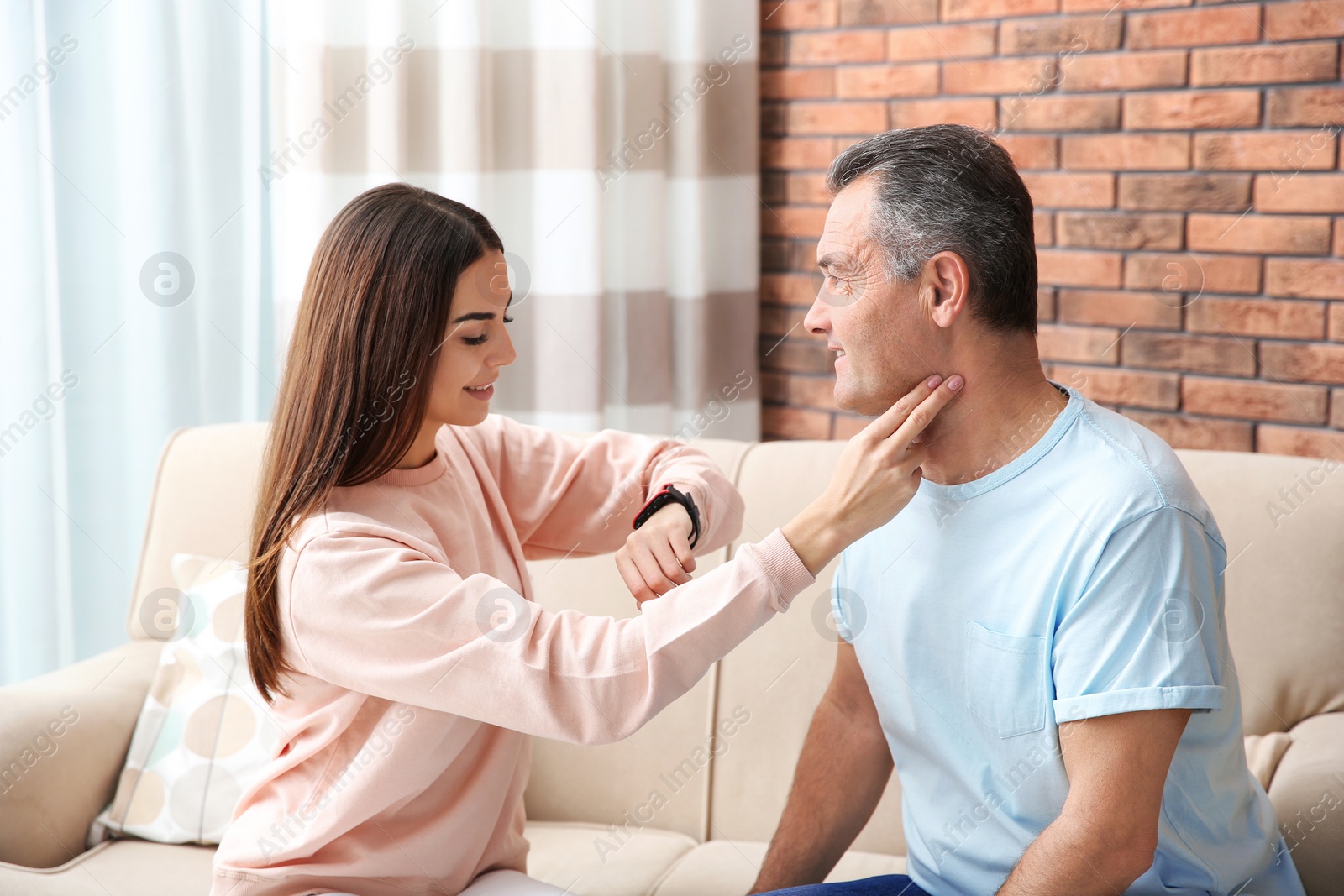 Photo of Young woman checking mature man's pulse with fingers at home