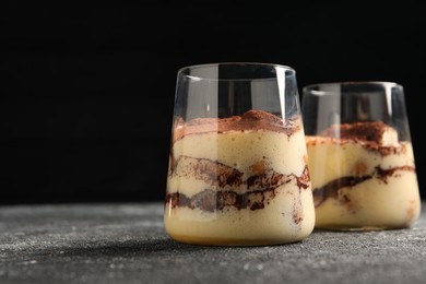 Delicious tiramisu in glasses on grey textured table, closeup. Space for text