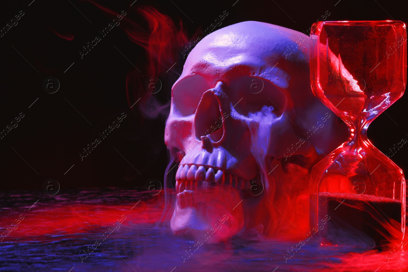 Photo of Human skull, hourglass and smoke in neon lights on black background. Space for text