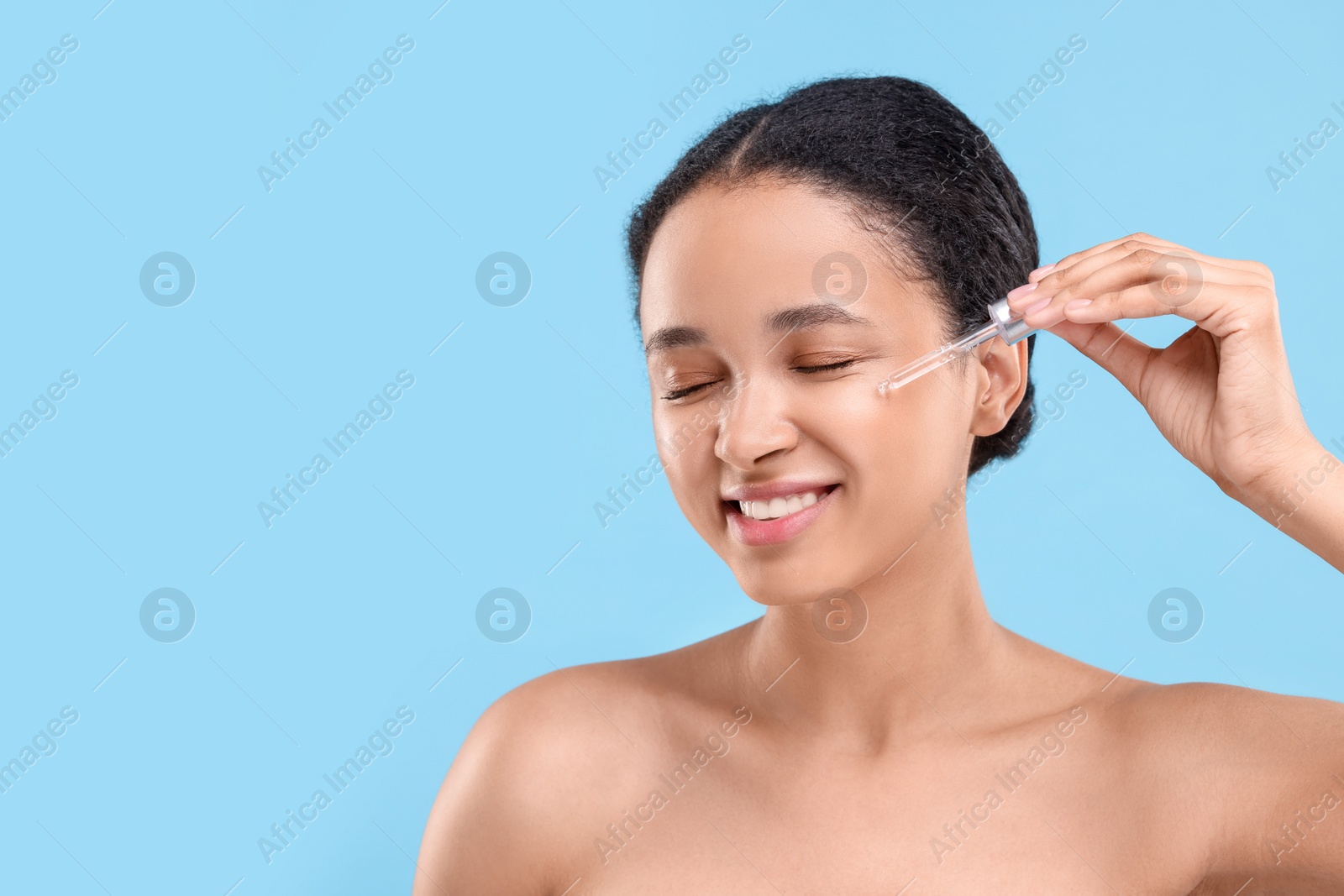 Photo of Smiling woman applying serum onto her face on light blue background. Space for text