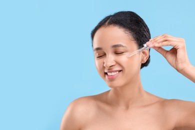 Smiling woman applying serum onto her face on light blue background. Space for text