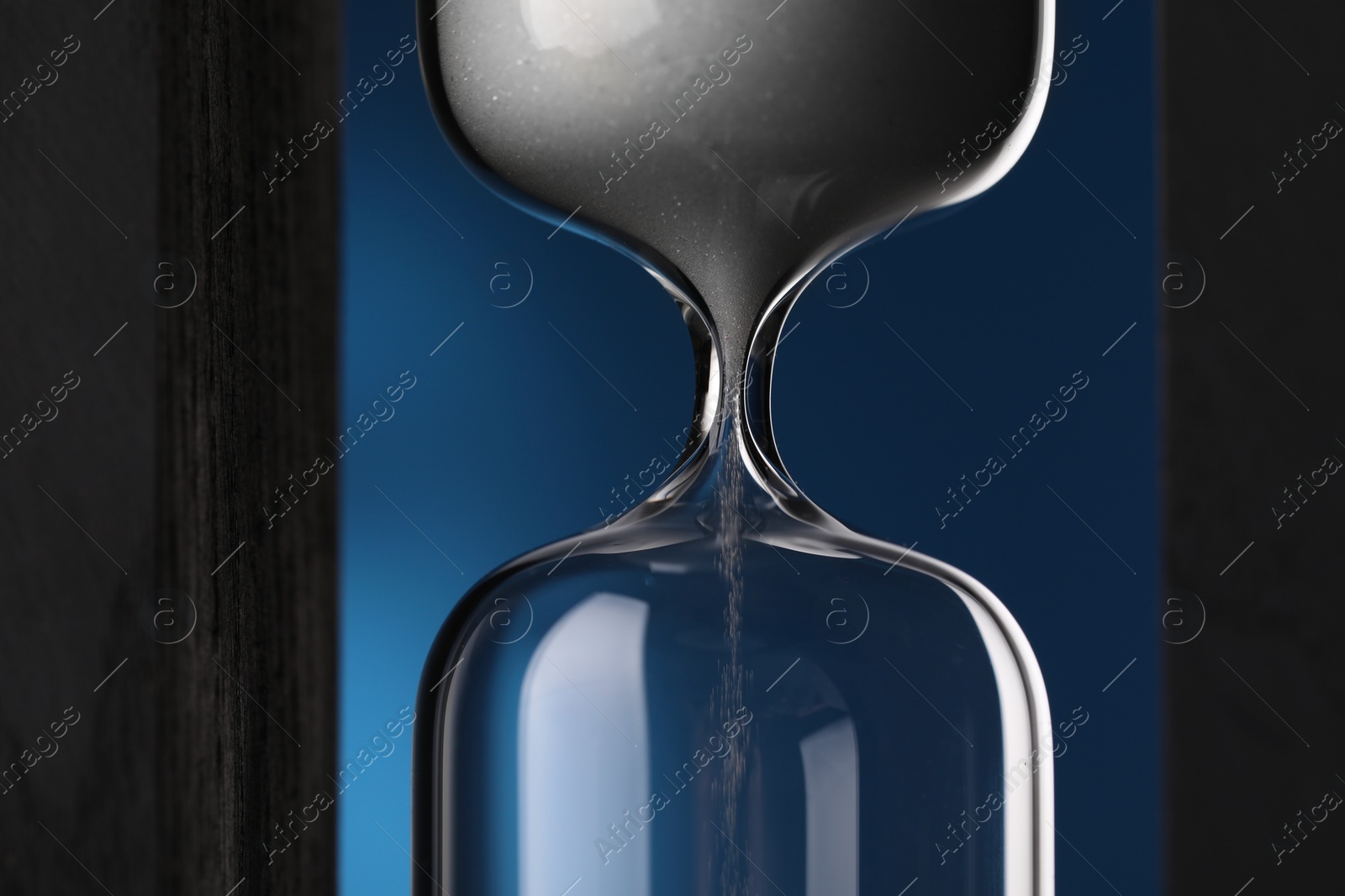 Photo of Hourglass with flowing sand on blue background, closeup