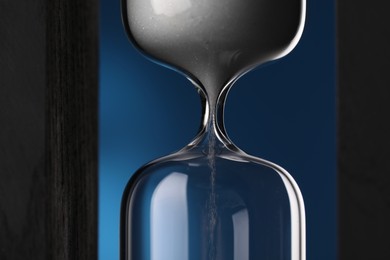Hourglass with flowing sand on blue background, closeup