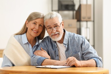 Smiling senior couple signing Last Will and Testament indoors