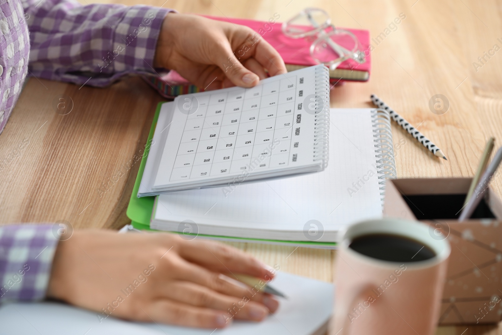 Photo of Woman with calendar at wooden table, closeup