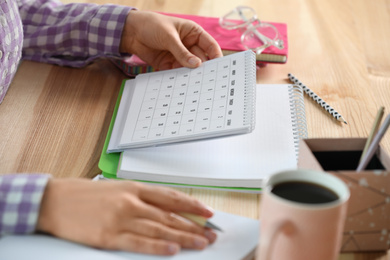 Photo of Woman with calendar at wooden table, closeup