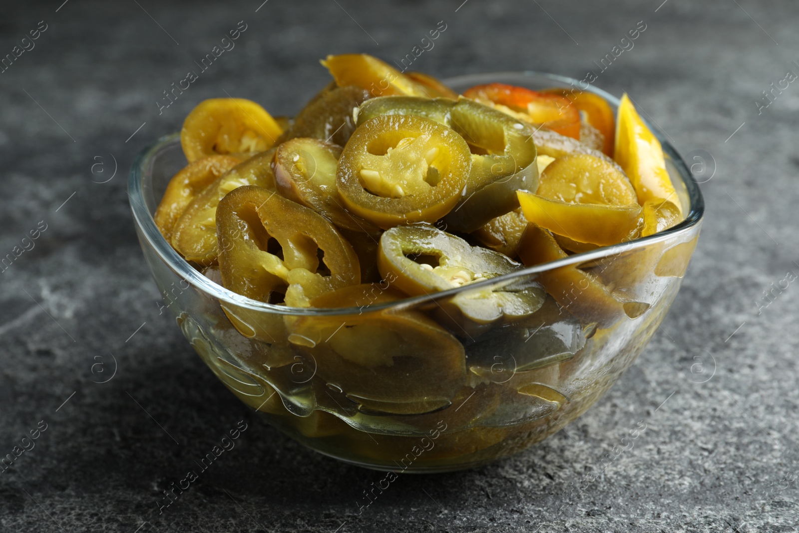 Photo of Glass bowl with slices of pickled green jalapeno peppers on grey table