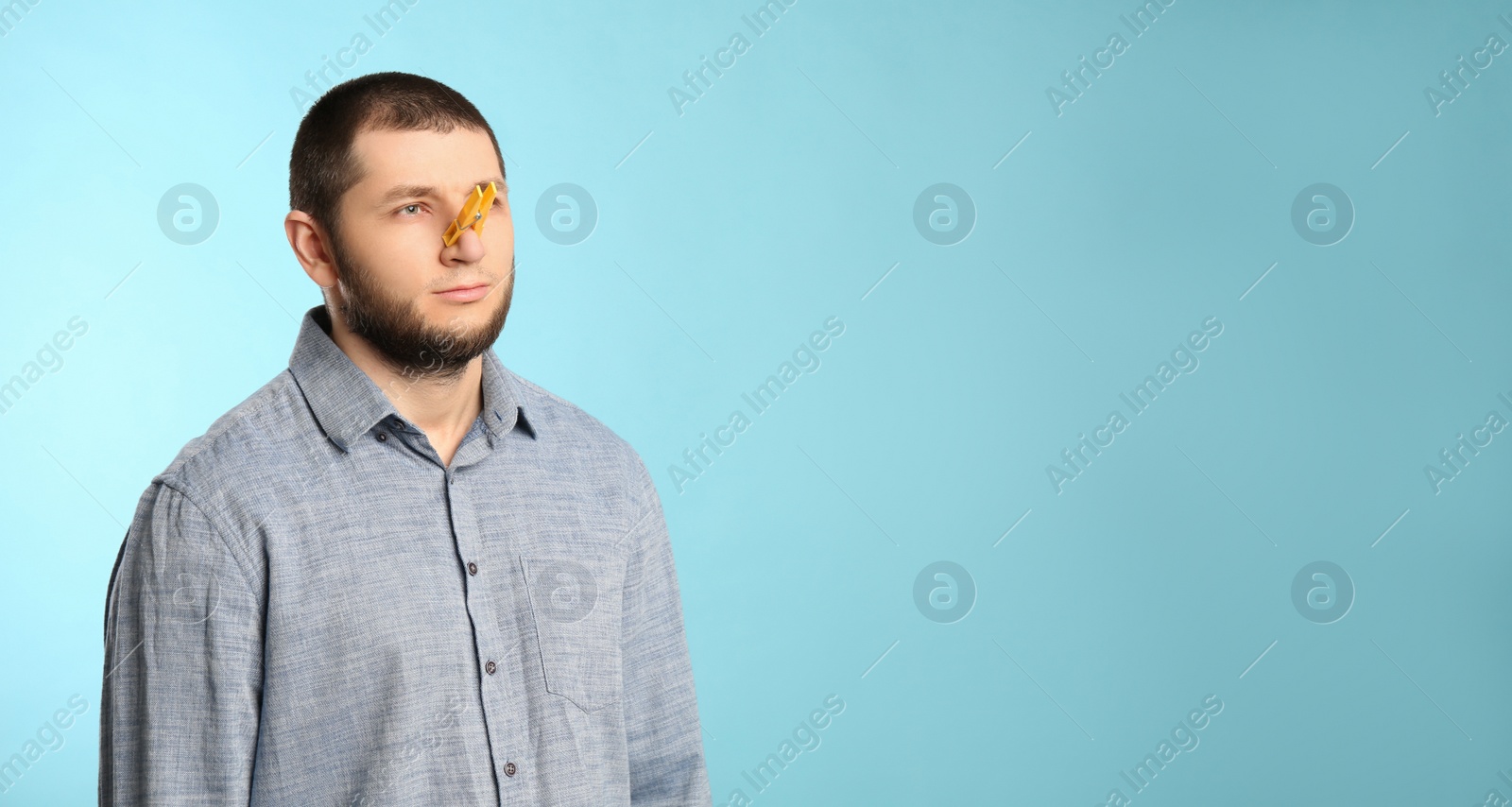 Photo of Man with clothespin on light blue background, space for text. Runny nose concept