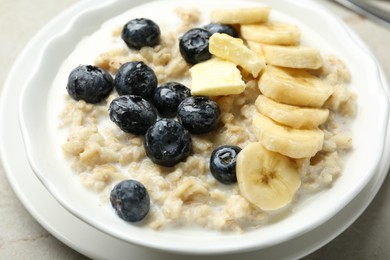 Tasty oatmeal with banana, blueberries, butter and milk served in bowl on light grey table, closeup