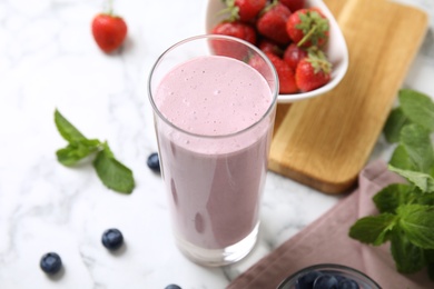 Photo of Tasty milk shake and berries on light table, closeup