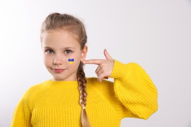 Photo of Little girl with drawing of Ukrainian flag on face against white background