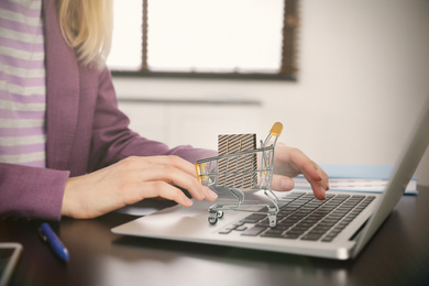 Image of Woman shopping online using laptop, small cart with bag on computer