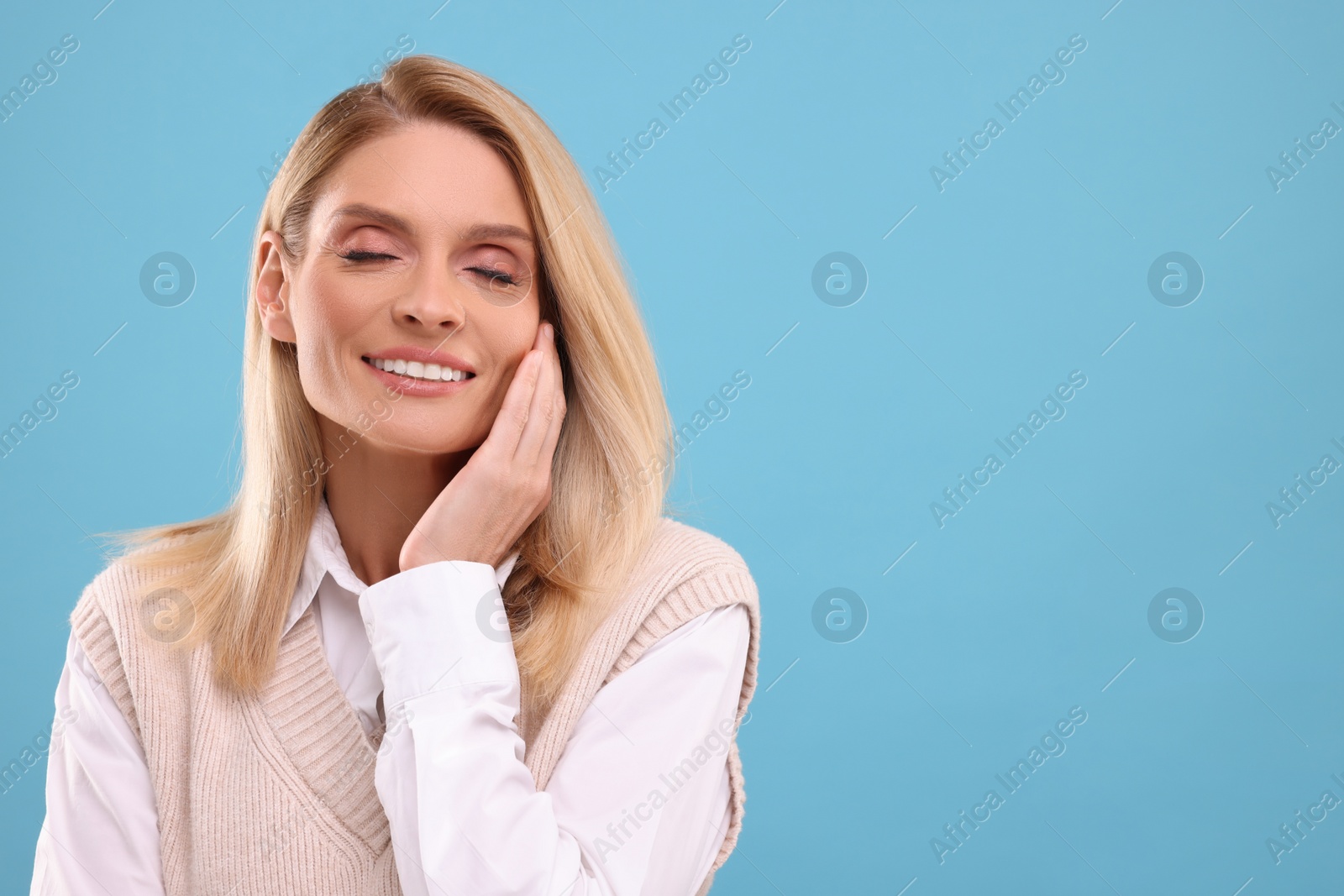 Photo of Portrait of smiling middle aged woman on light blue background. Space for text