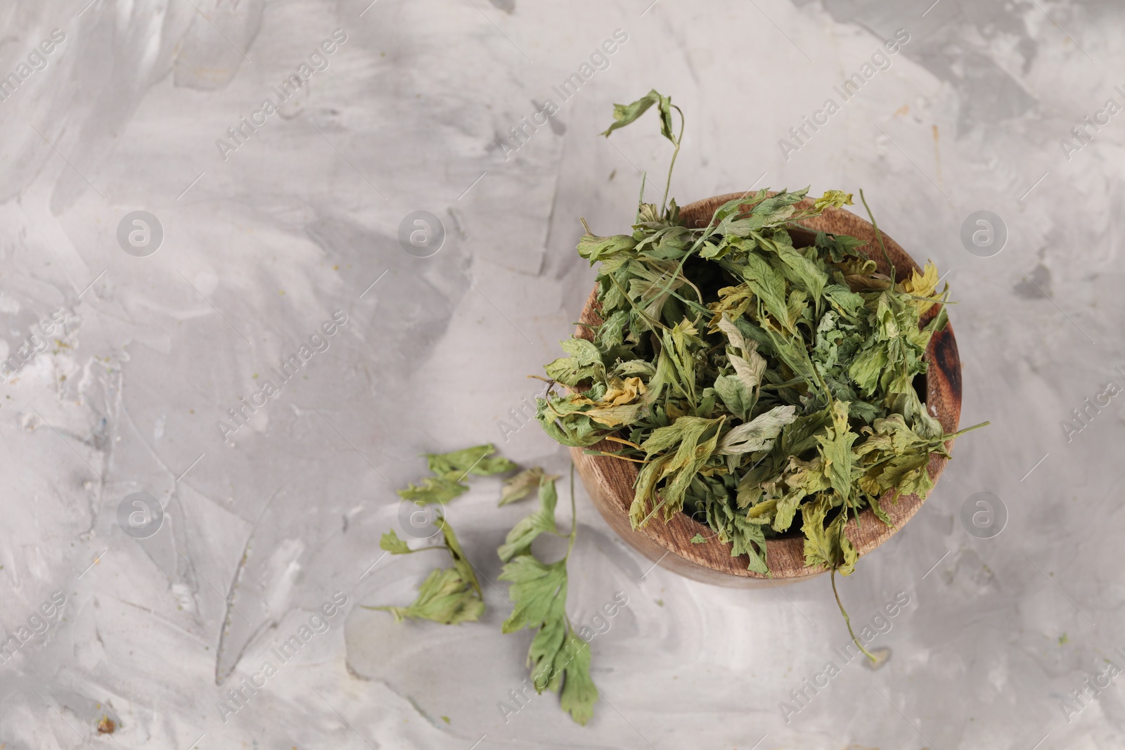 Photo of Bowl with dry parsley on light grey textured table, flat lay. Space for text