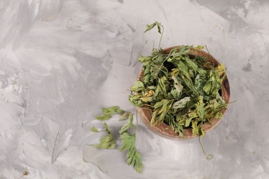 Bowl with dry parsley on light grey textured table, flat lay. Space for text