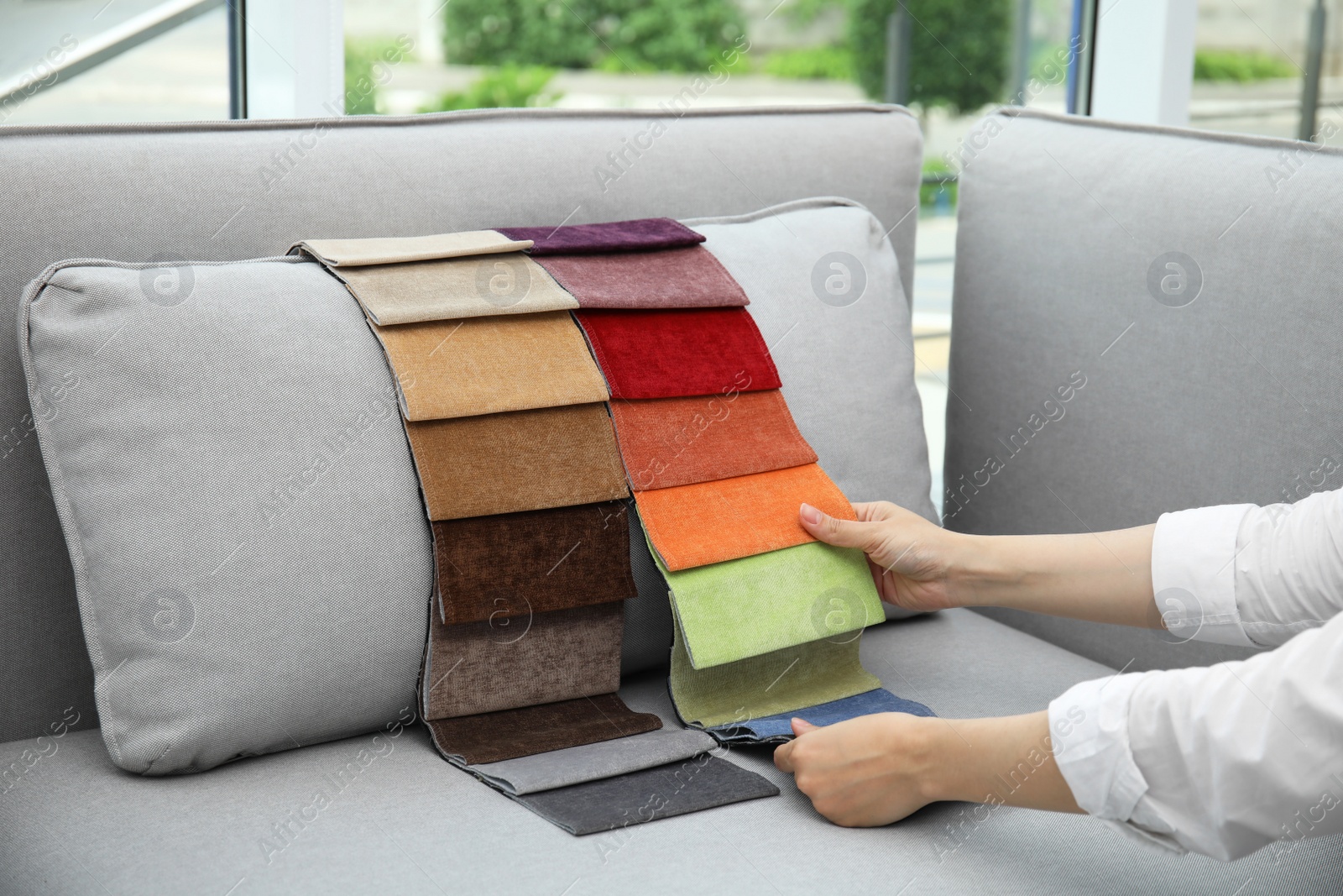 Photo of Woman choosing fabric among colorful samples on grey sofa at home, closeup