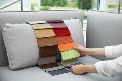 Photo of Woman choosing fabric among colorful samples on grey sofa at home, closeup