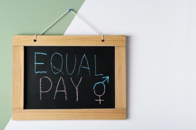 Photo of Blackboard with words Equal Pay and gender symbols hanging on color wall. Space for text