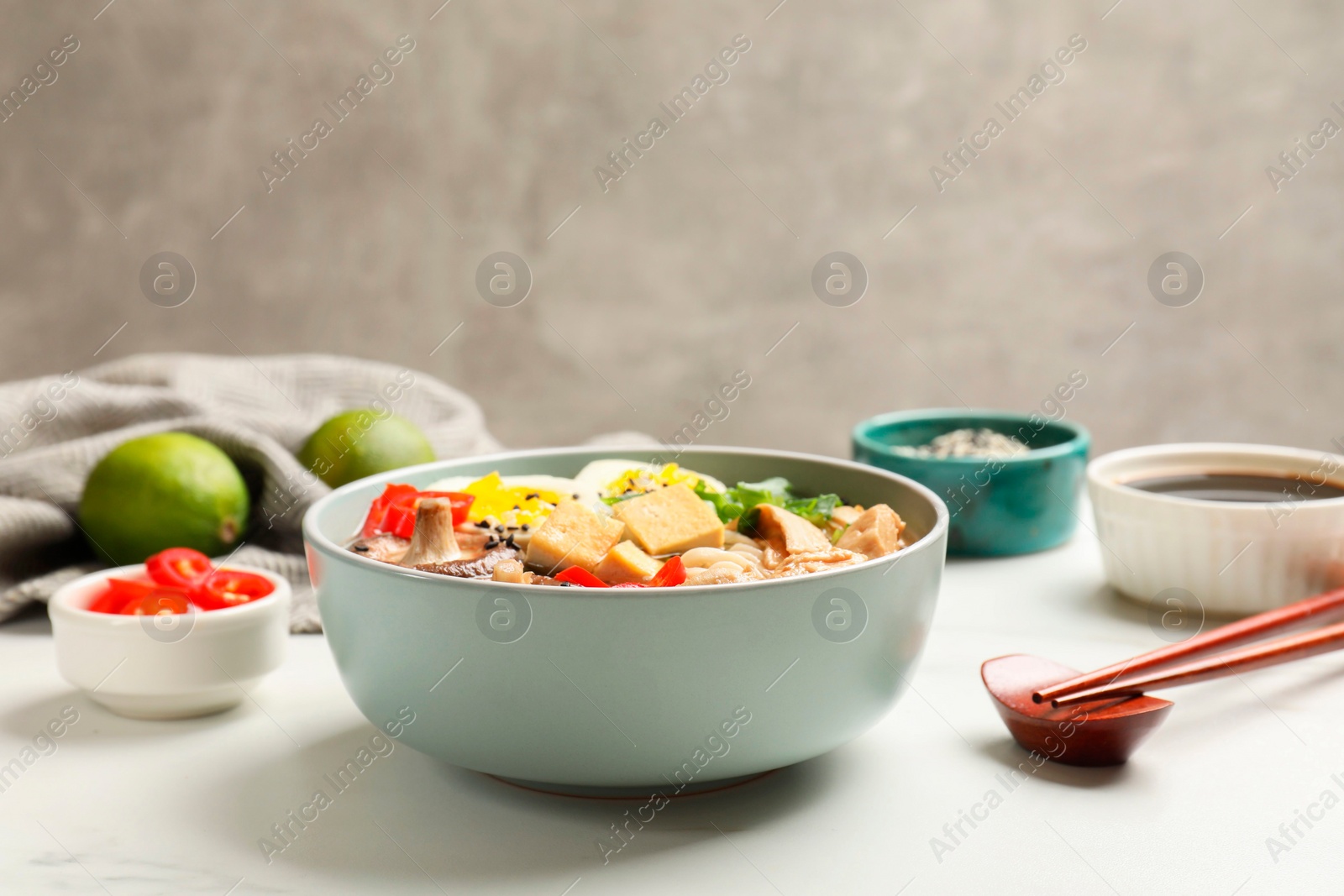 Photo of Bowl of delicious ramen, ingredients and chopsticks on white table, closeup. Noodle soup