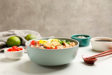 Photo of Bowl of delicious ramen, ingredients and chopsticks on white table, closeup. Noodle soup