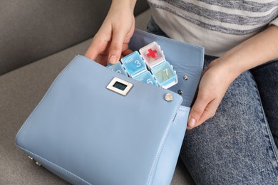 Photo of Woman putting pill box into bag on sofa, closeup