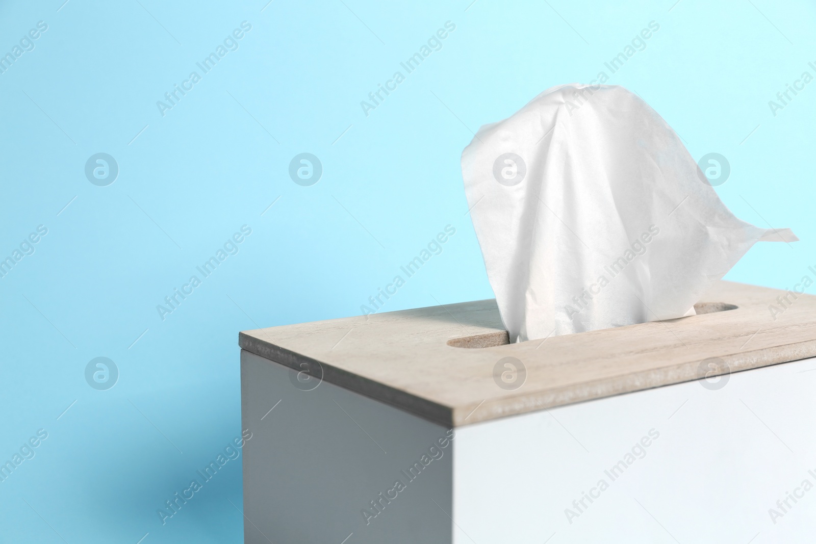 Photo of Holder with paper tissues on light blue background, closeup