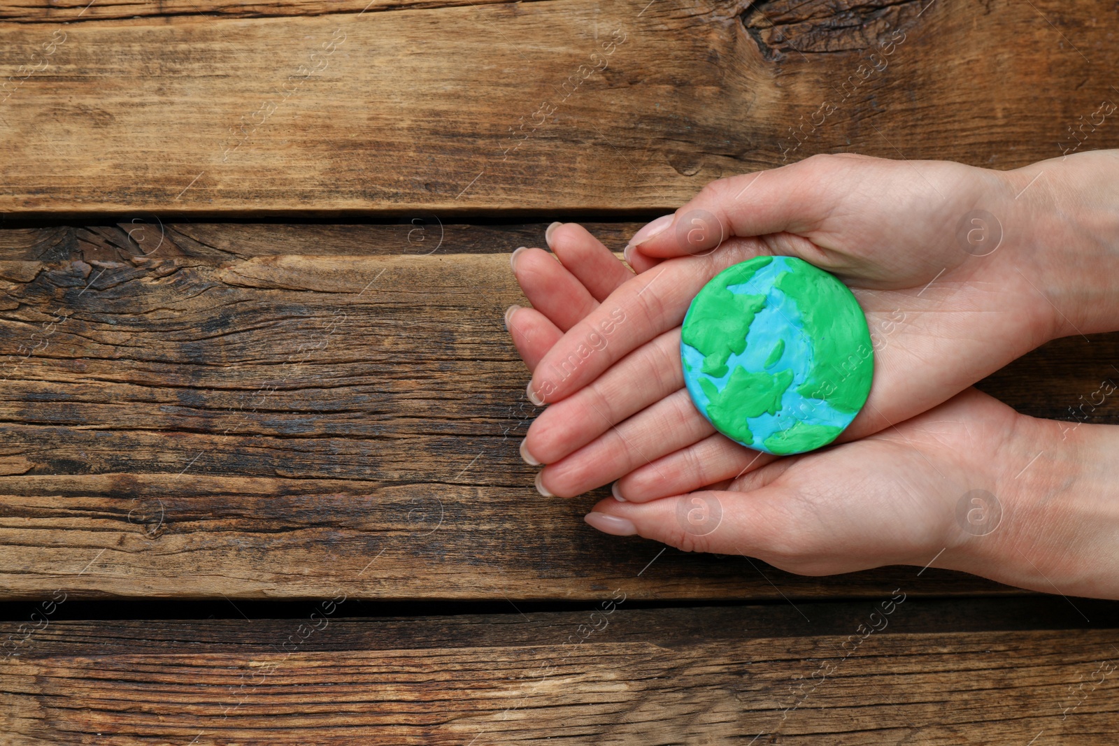 Photo of Happy Earth Day. Woman with plasticine planet at wooden table, top view and space for text