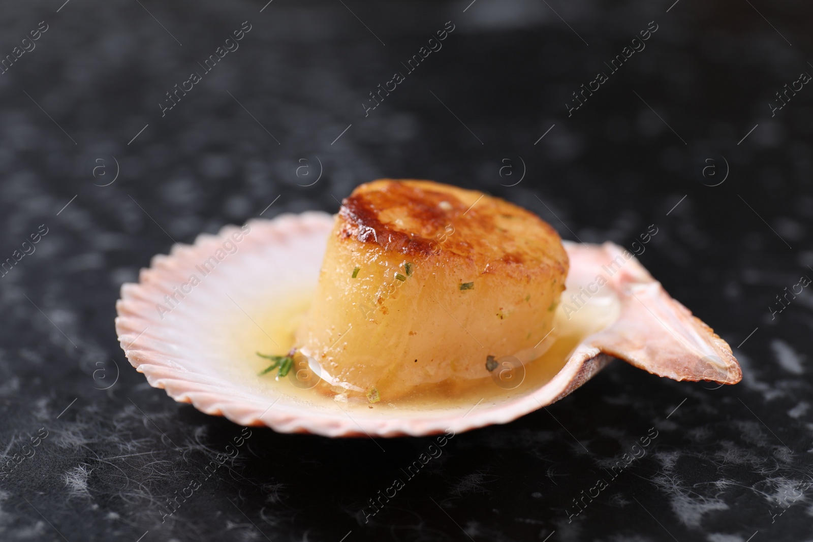 Photo of Delicious fried scallop in shell on black table, closeup