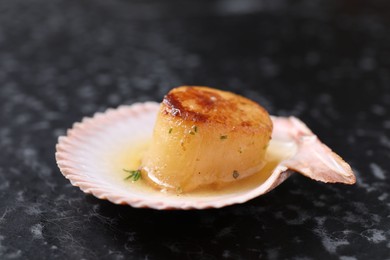 Photo of Delicious fried scallop in shell on black table, closeup