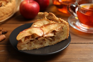 Photo of Slice of delicious apple pie served with tea on wooden table, closeup