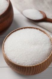 Photo of Granulated sugar in bowl on white wooden table, closeup