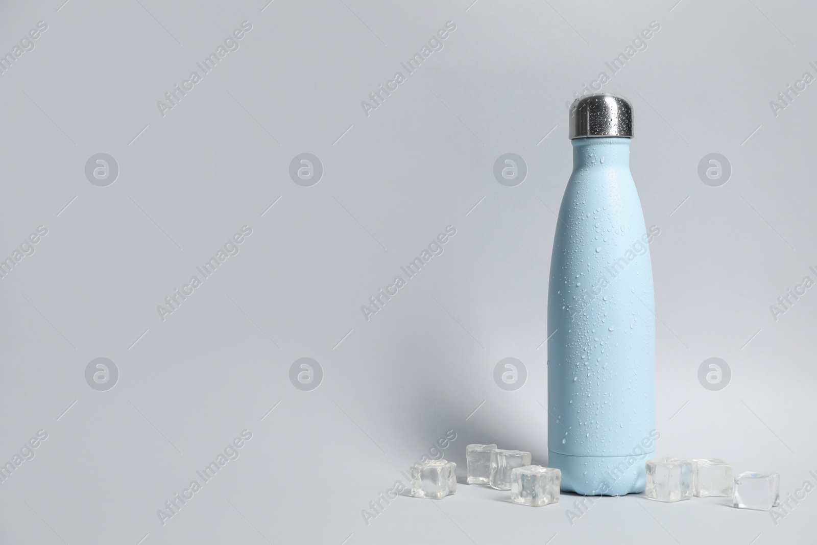 Photo of Stylish closed thermo bottle with water drops on light grey background, space for text