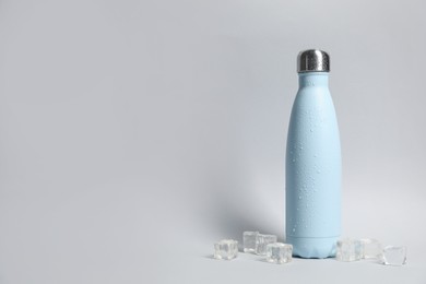 Photo of Stylish closed thermo bottle with water drops on light grey background, space for text