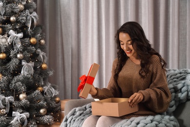 Image of Happy young woman opening Christmas gift at home