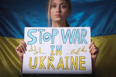 Photo of Sad woman holding poster with words Stop War in Ukraine near national flag