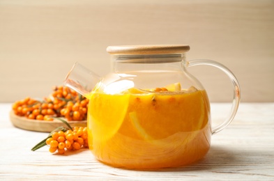 Photo of Delicious sea buckthorn tea with orange slices and fresh berries on white wooden table