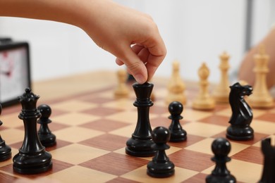 Photo of Little child playing chess indoors, closeup view
